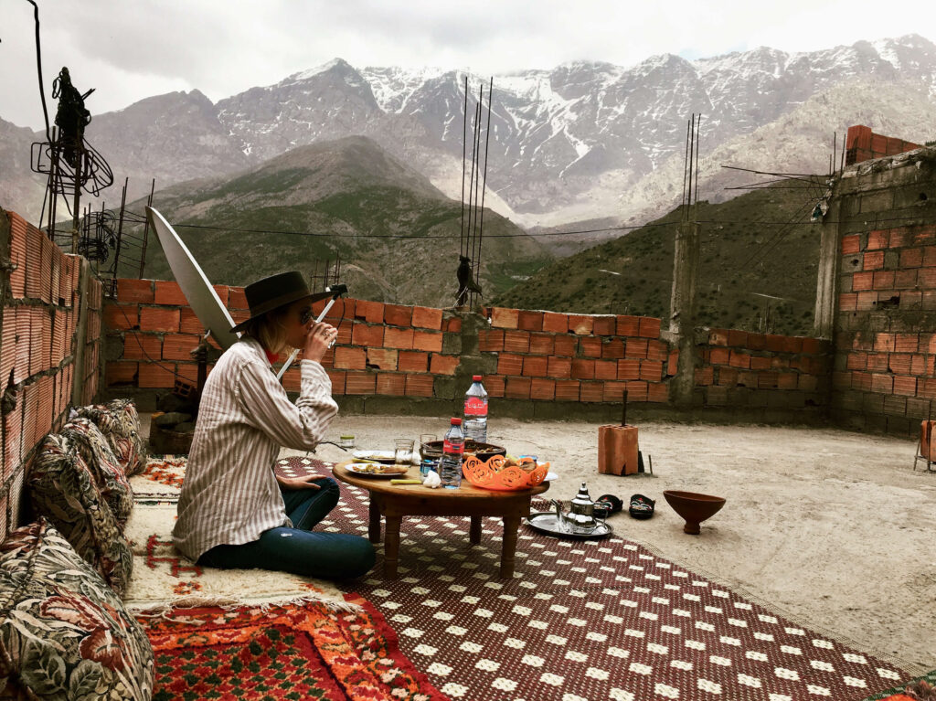 Woman drinking tea on a rooftop terrace in the Atlas Mountains, Morocco, surrounded by rugs and traditional decor