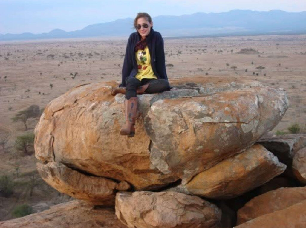 Woman sitting on a large rock formation overlooking the vast savanna landscape in East Africa during golden hour