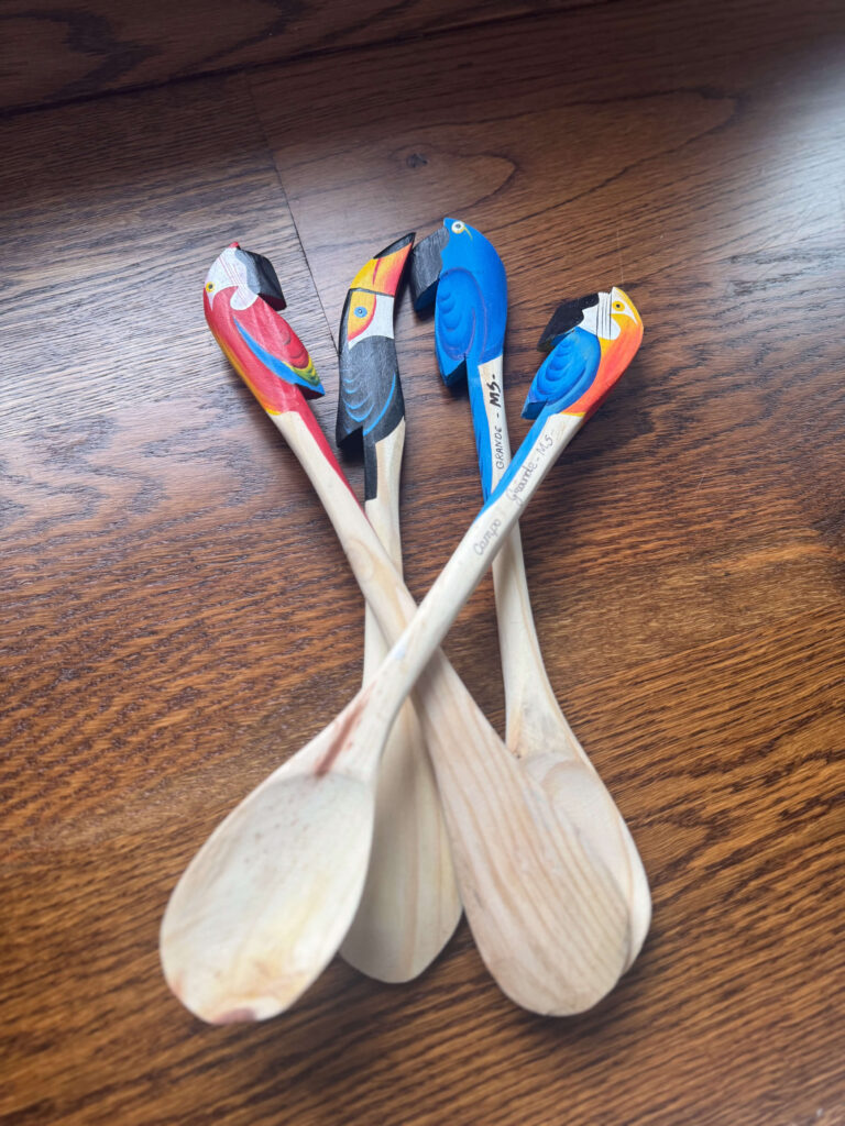 A set of hand-carved wooden spoons with parrot heads painted in bright colors, each marked with the location “Grace Guatemala MJS.”