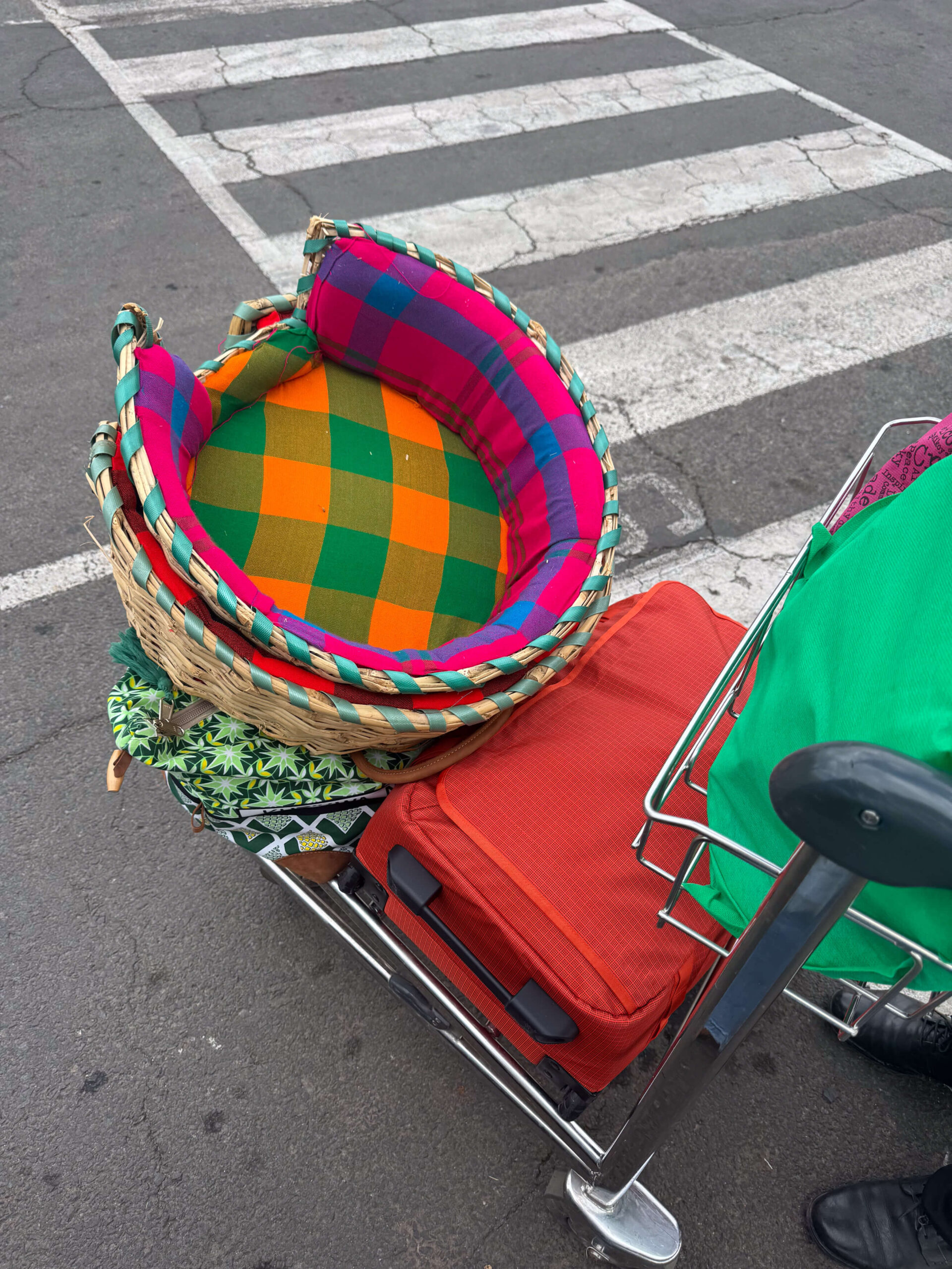 Colorful dog beds woven from basketry material, stacked on top of a luggage trolley at the airport.