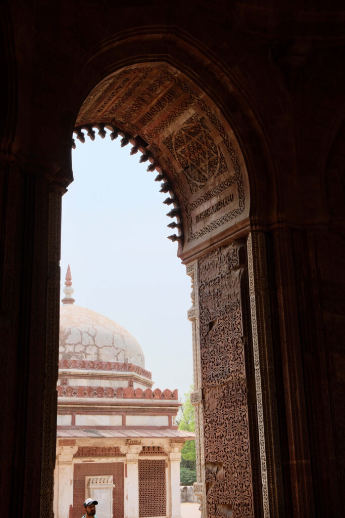 View through ornate arched doorway framing a historic dome structure in India, showcasing intricate stone carvings.