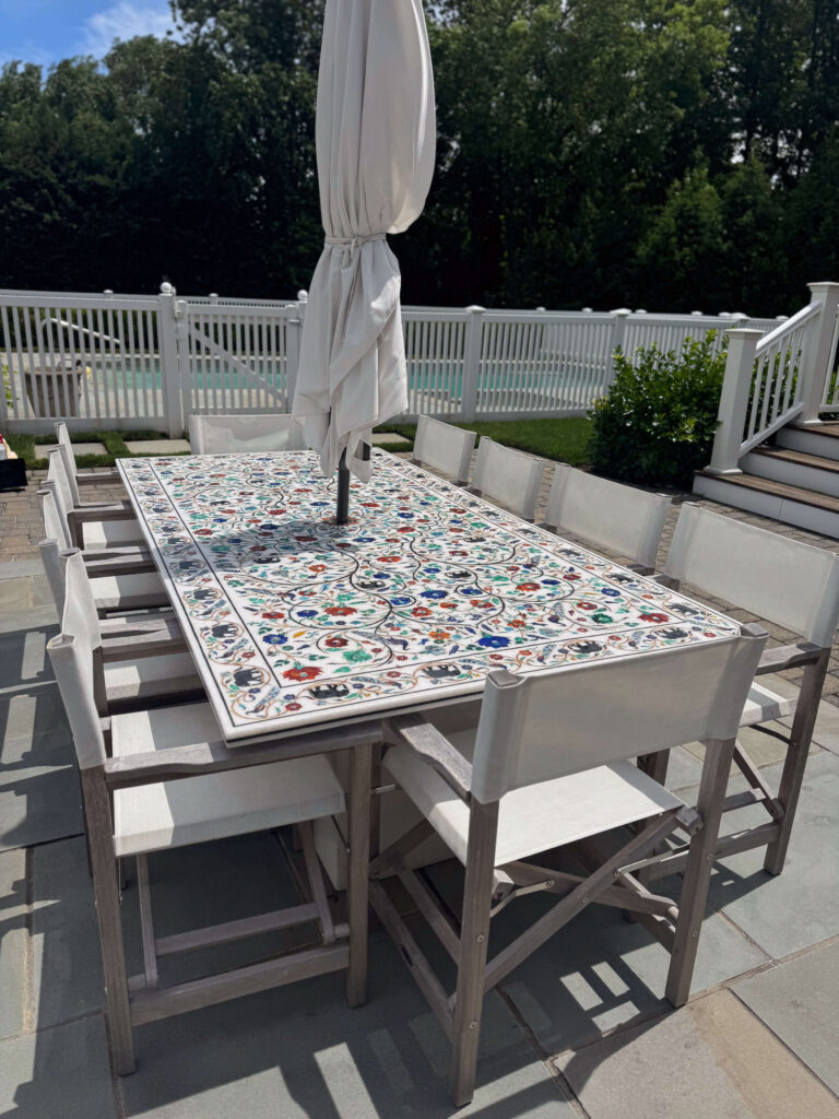 Outdoor dining table with intricate inlaid marble top featuring colorful floral patterns, set on a stone patio.