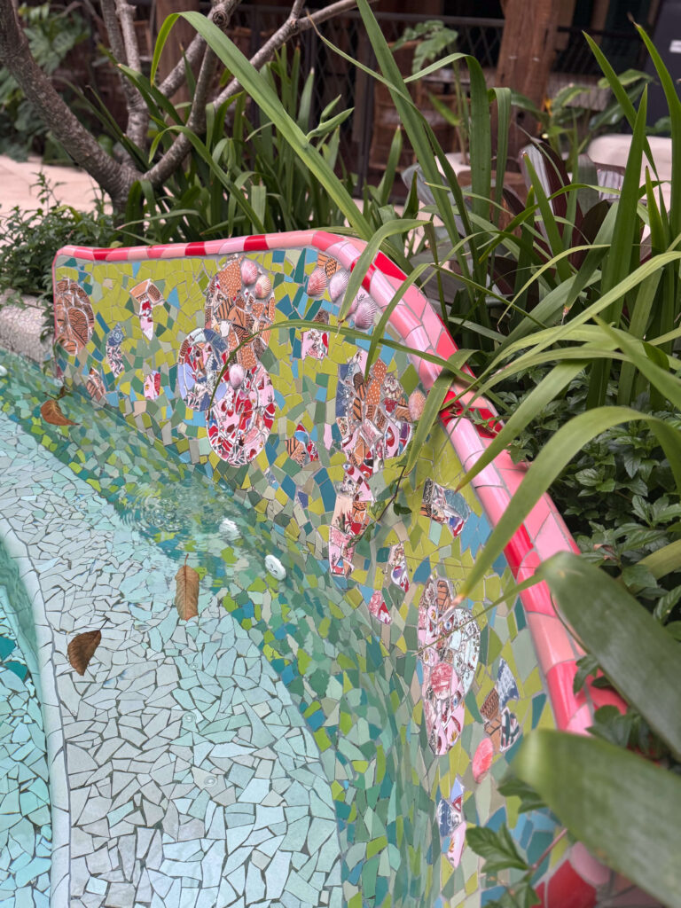 Mosaic-tiled pool edge surrounded by lush greenery.