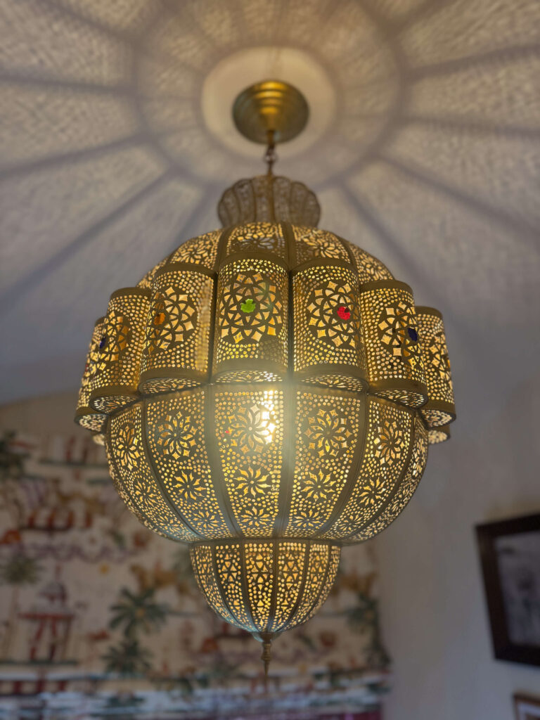 A large, ornate Moroccan-style chandelier casts intricate light patterns on the ceiling, with colorful inlaid glass details.