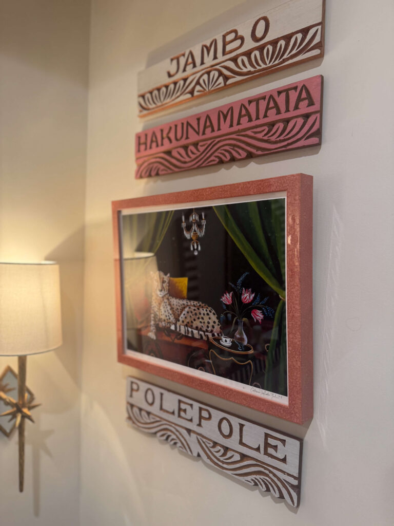 Wall decor with hand-carved Swahili signs reading “Jambo,” “Hakuna Matata,” and “Polepole,” surrounding a framed cheetah artwork.