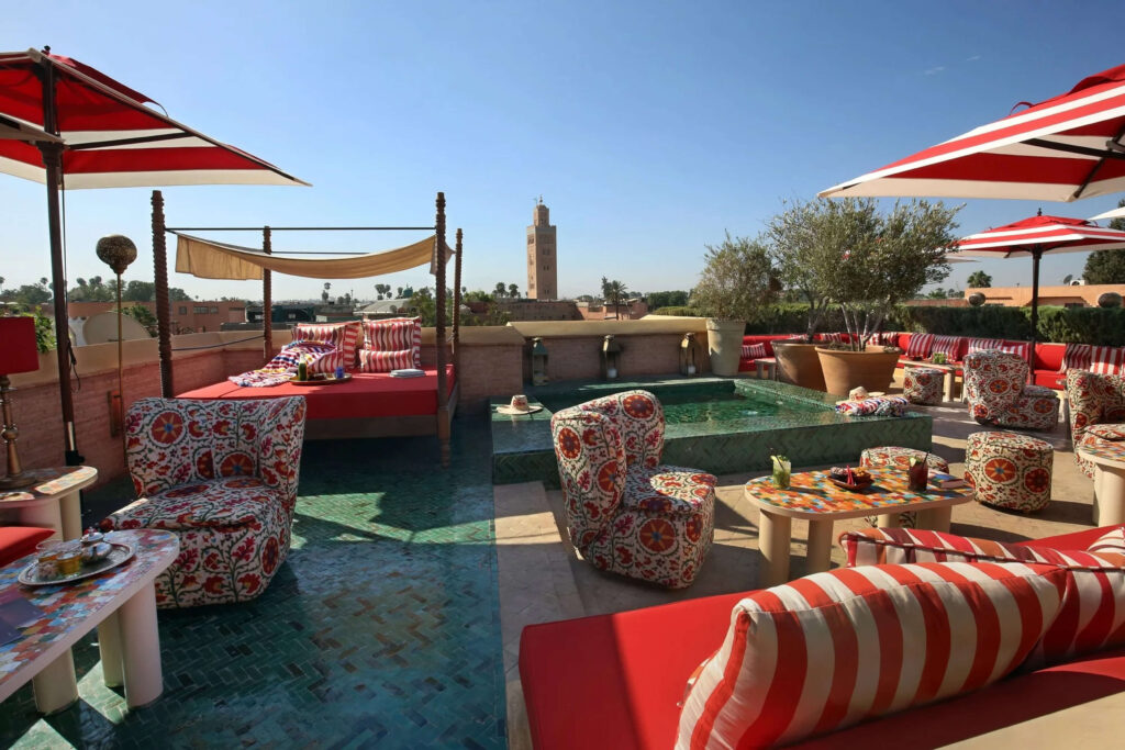 Chic rooftop lounge at El Fenn in Marrakech, with striped daybeds, colorful decor, and views of the Koutoubia Mosque