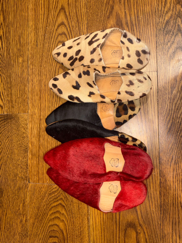 Collection of Moroccan babouche slippers in red, black, and animal print on a wooden floor